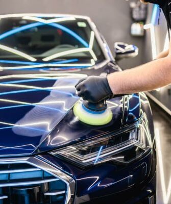 Car detailing - Man with orbital polisher in repair shop polishing car. Selective focus.